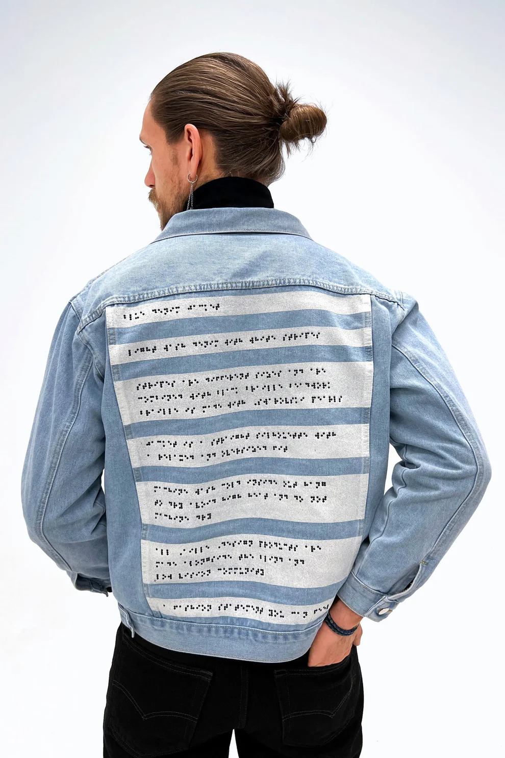 man wears pale blue denim jacket and shows back with braille giving description of jacket of jacket with 